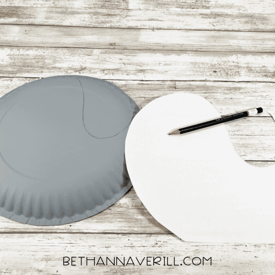A gray-painted paper plate with a seal body shape lightly sketched in pencil next to a white paper template.