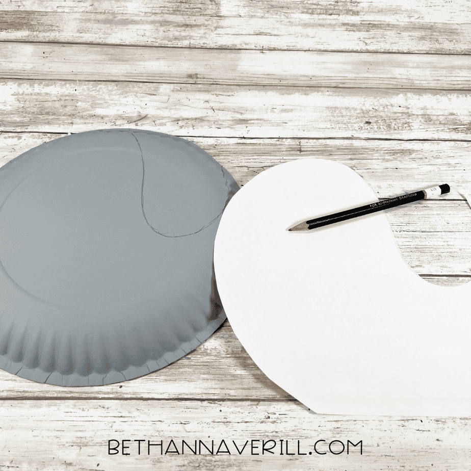 A gray-painted paper plate with a seal body shape lightly sketched in pencil next to a white paper template.