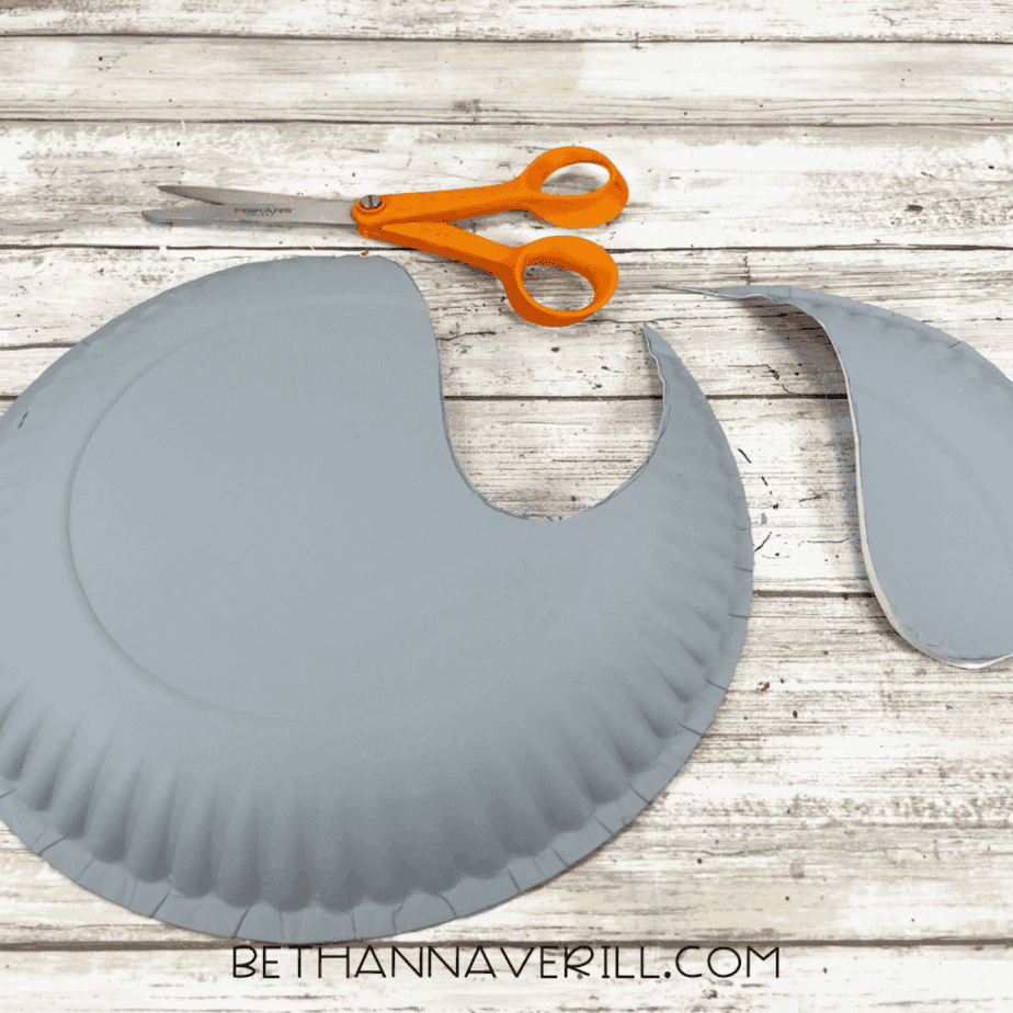 A cut gray paper plate showing the seal body shape with a large section removed and scissors nearby.