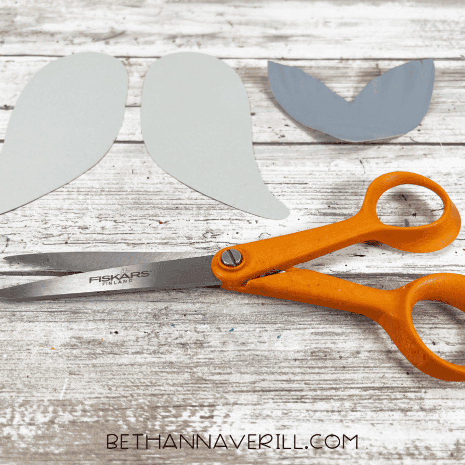 Cut gray cardstock flippers and tail pieces placed beside orange scissors.