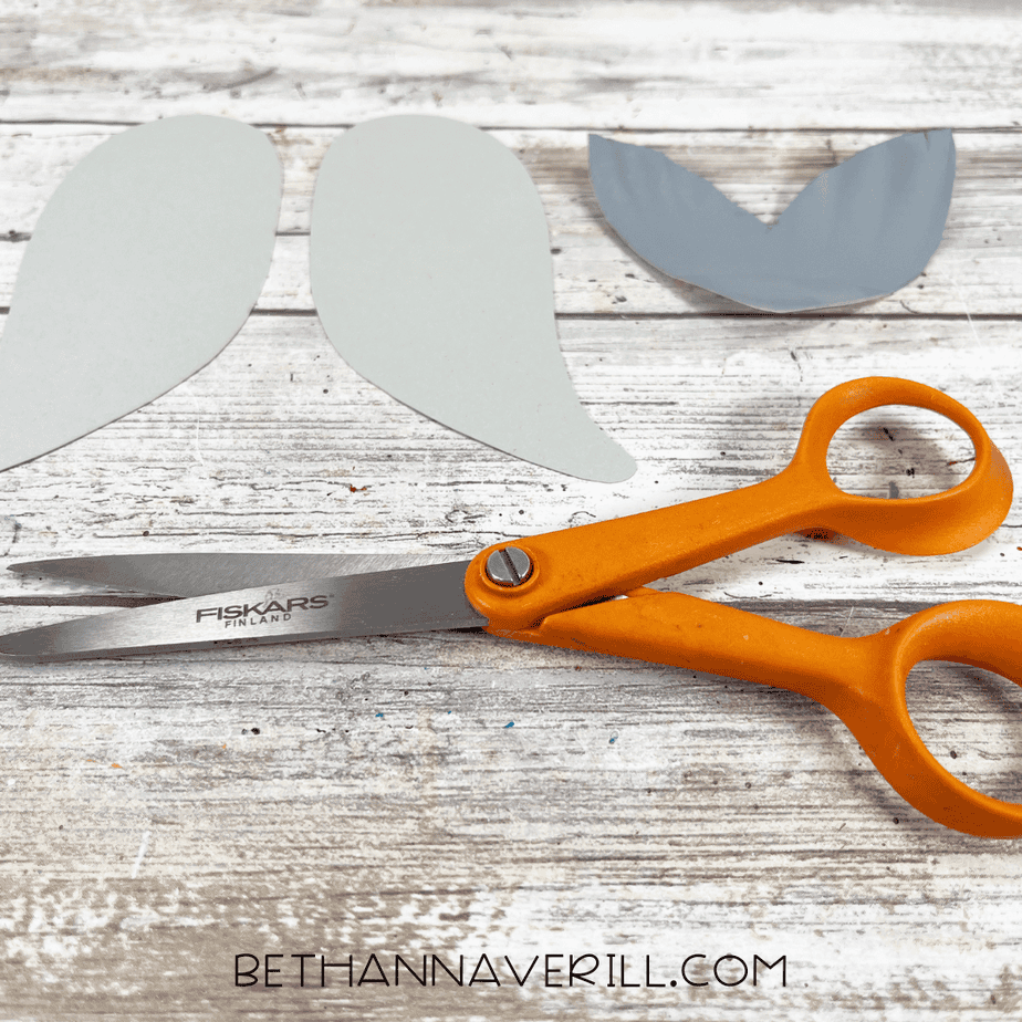 Cut gray cardstock flippers and tail pieces placed beside orange scissors.