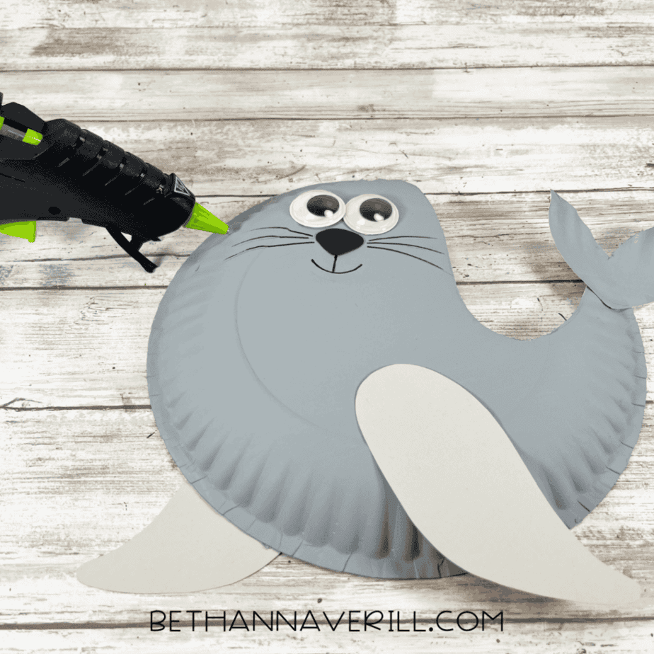 A paper plate seal with googly eyes added and whiskers drawn on using a black marker.