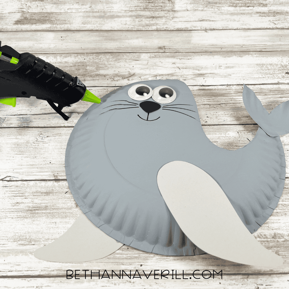A paper plate seal with googly eyes added and whiskers drawn on using a black marker.