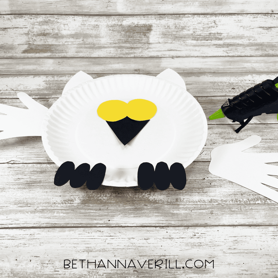 Cute paper plate turkey craft for Thanksgiving, featuring black, yellow, and white paper elements, with glue gun and paper hands for a fun holiday decoration or kids' craft activity.