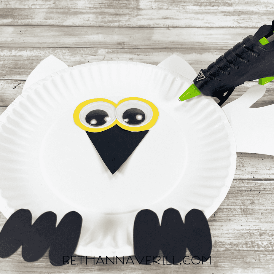 Googly eyes being glued onto the snowy owl’s yellow eye circles on the paper plate.