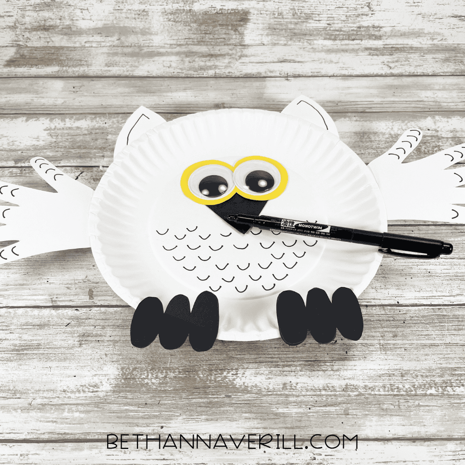 Black marker adding small curved feather markings to the snowy owl paper plate craft.