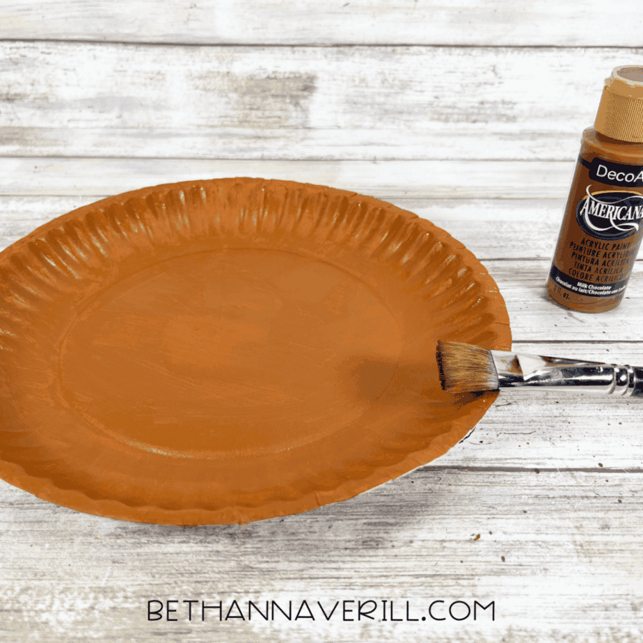 Paper plate painted brown for the base of the walrus craft, with a paintbrush and brown paint bottle beside it.