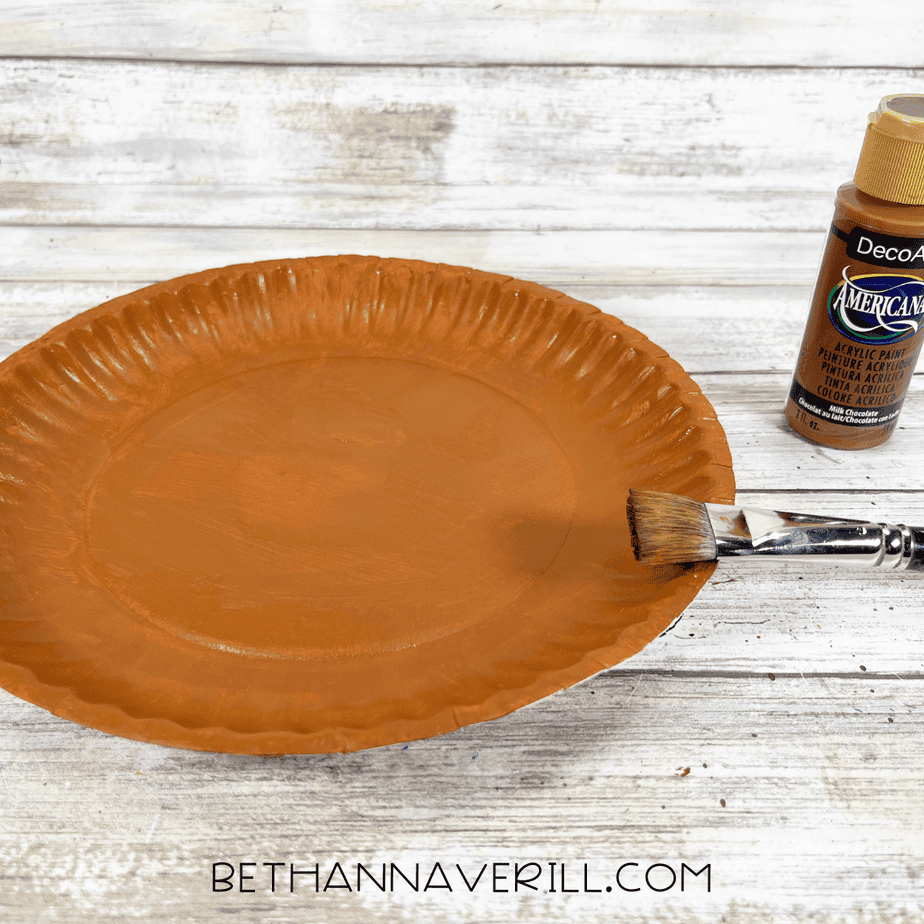 Paper plate painted brown for the base of the walrus craft, with a paintbrush and brown paint bottle beside it.