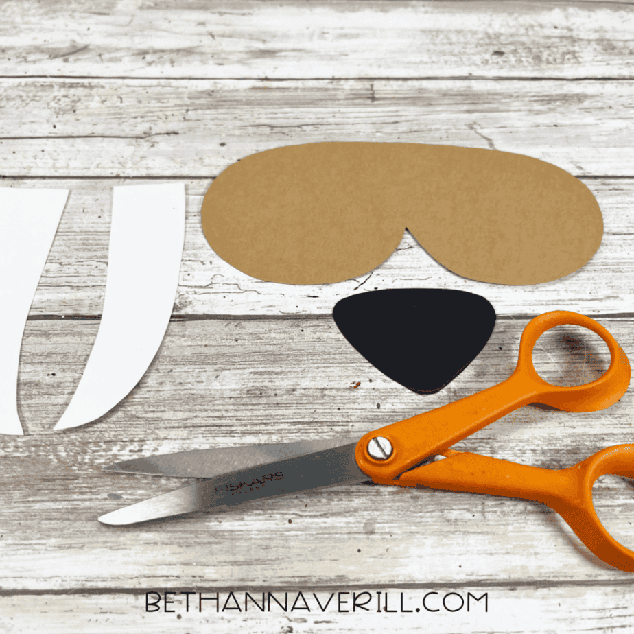 Cut-out walrus face pieces and tusks laid out next to orange scissors.