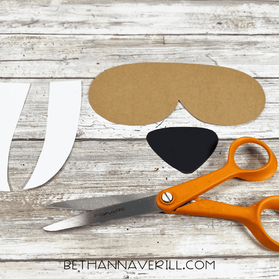 Cut-out walrus face pieces and tusks laid out next to orange scissors.