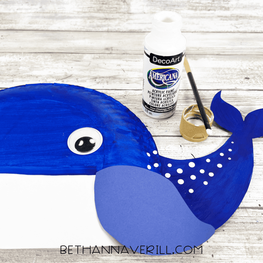 White acrylic paint being used to add dotted details to the whale’s tail with a small round paintbrush.
