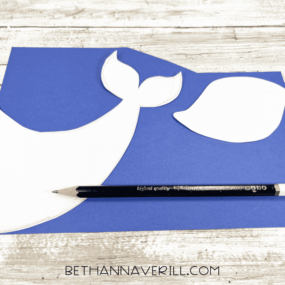 Whale tail and fin templates traced onto blue cardstock using a pencil.