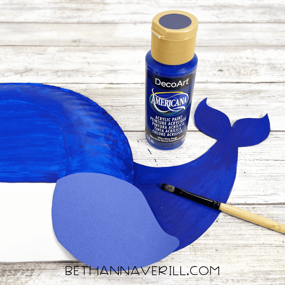 Blue acrylic-painted whale with cardstock tail being painted with matching blue paint to blend the pieces together.