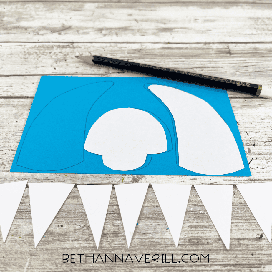 Yeti horn and face templates traced onto blue cardstock with a pencil, with white triangle teeth pieces lined up below.