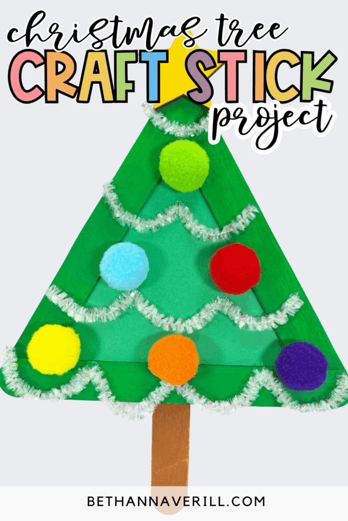 Popsicle stick Christmas tree craft on a light background, decorated with green craft sticks, pom poms, silver pipe cleaner garland, and a yellow star, with text overlay reading “christmas tree craft stick project.”