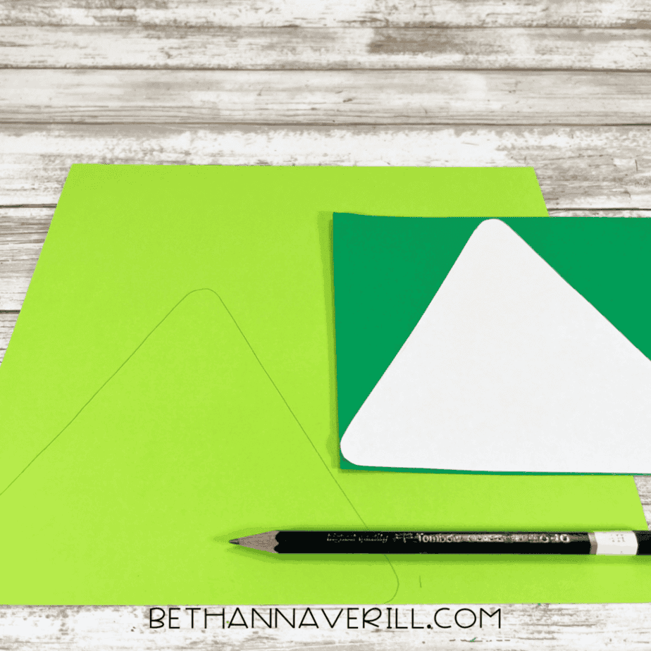 Light and dark green cardstock with a triangle shape traced in pencil, alongside a pencil and stacked cardstock.