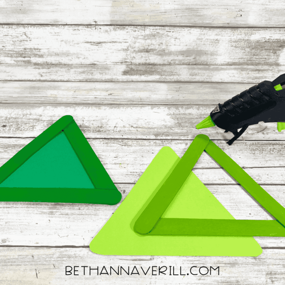 Painted popsicle stick triangles glued onto green cardstock triangles, showing the layered tree shape before decoration.