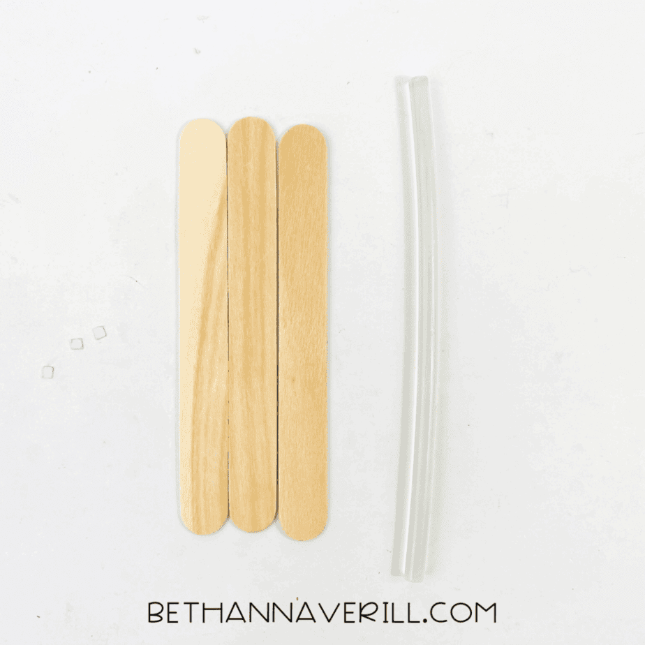 Three jumbo craft sticks lined up vertically next to two clear glue gun sticks on a white background.