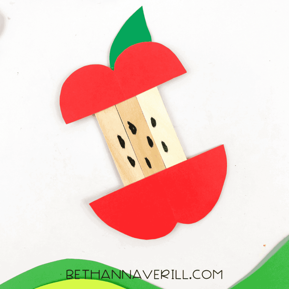 Finished apple popsicle stick craft with red cardstock apple shape, green leaf, and black seed details on the sticks.