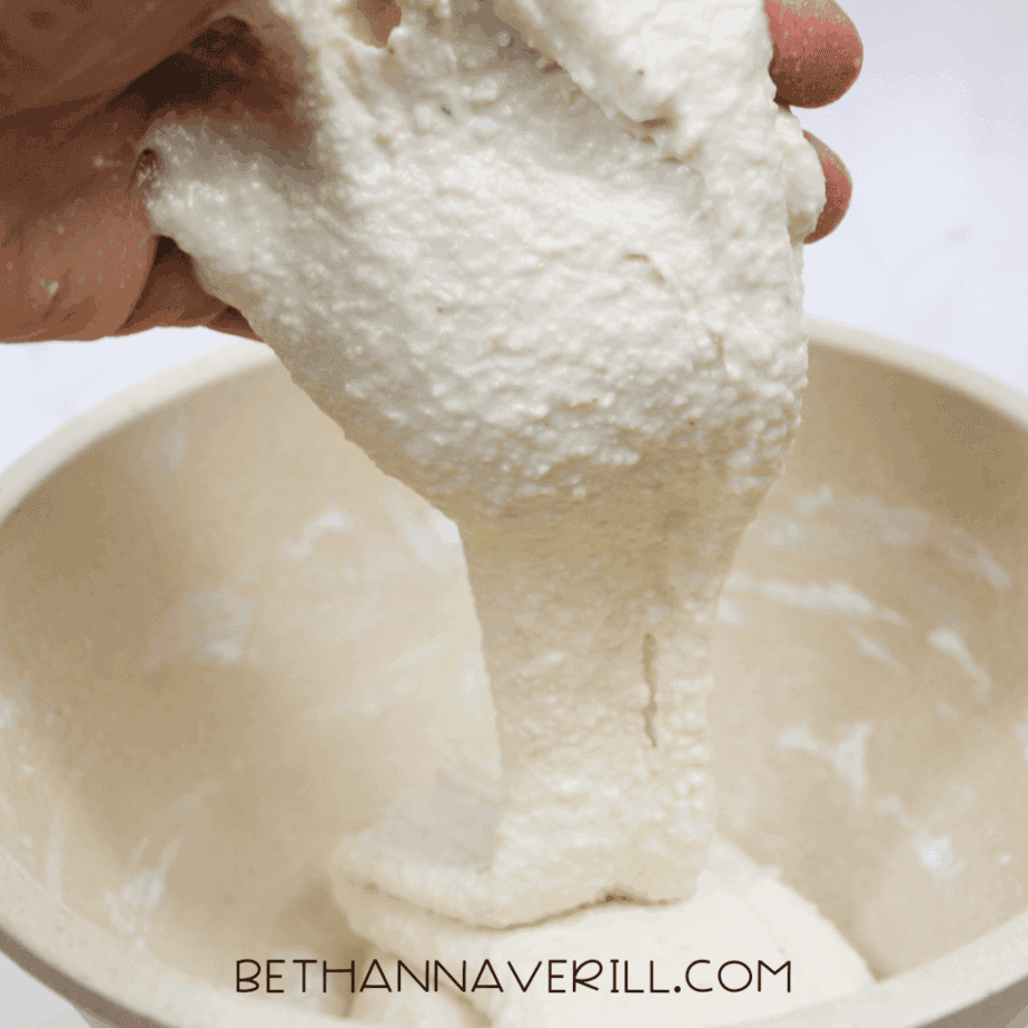 Hand lifting stretchy applesauce slime from a mixing bowl to show texture.