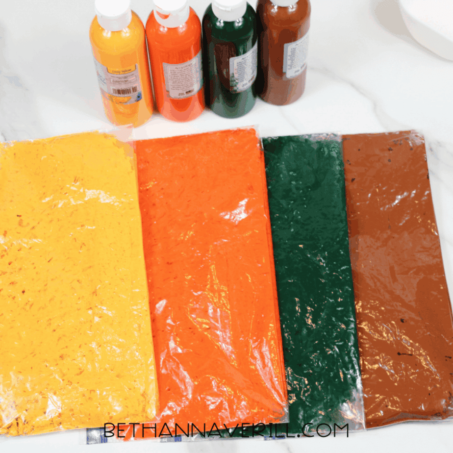 Zip-top bags filled with dyed beans in yellow, orange, green, and brown for a fall sensory bin.