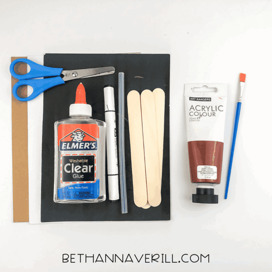 Craft supplies laid out on a white background including scissors, clear glue, black marker, glue stick, hot glue stick, jumbo craft sticks, brown and black cardstock, and brown acrylic paint with a paintbrush.