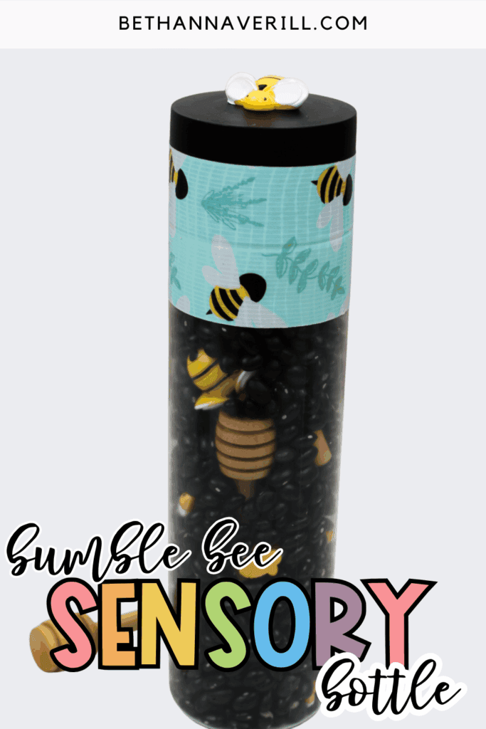Finished bumble bee sensory bottle filled with black beans, small bee figures, and a wooden honey dipper inside a clear bottle with a black lid.