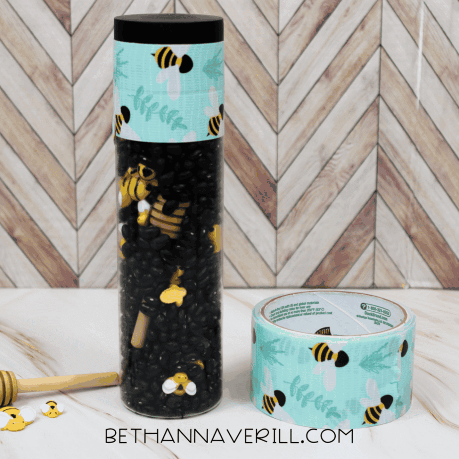 Completed bumble bee sensory bottle next to a roll of bee-themed decorative tape and loose bee figures.