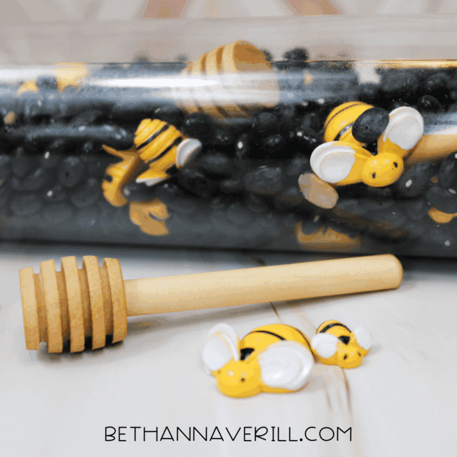Bumble bee sensory bottle lying on its side with black beans, bee figures, and a honey dipper visible inside.