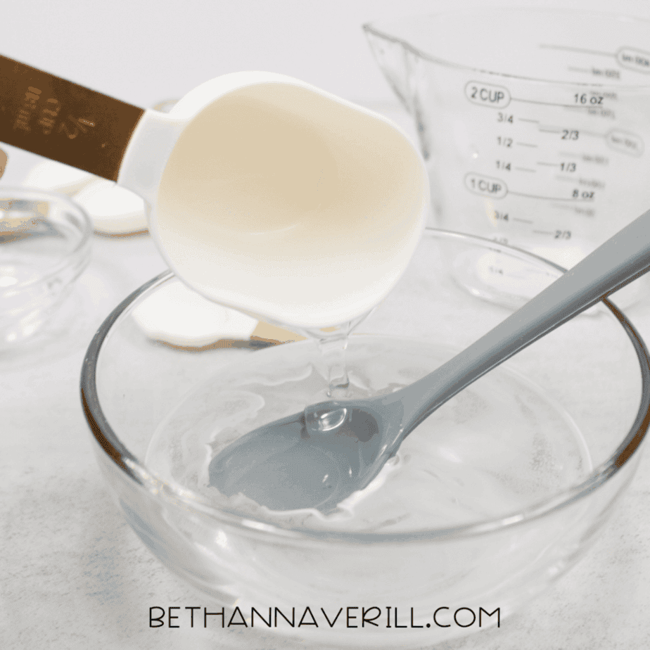 Measuring cup pouring a milky white liquid into a glass bowl with a silicone spoon.