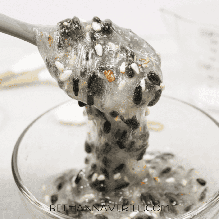 Close-up of birdseed slime mixture stretched upward from a glass bowl on a silicone spoon.