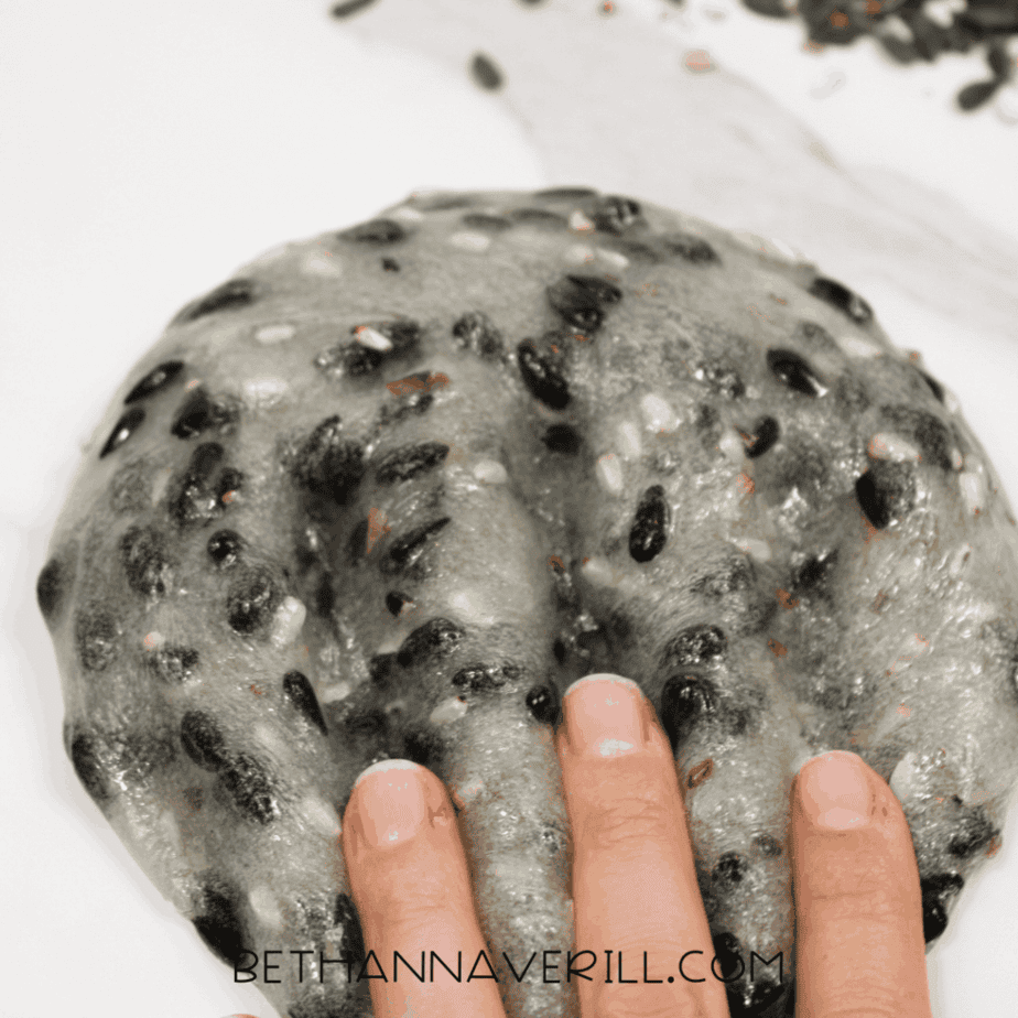 Hand pressing fingers into a flattened mound of birdseed slime on a white surface.