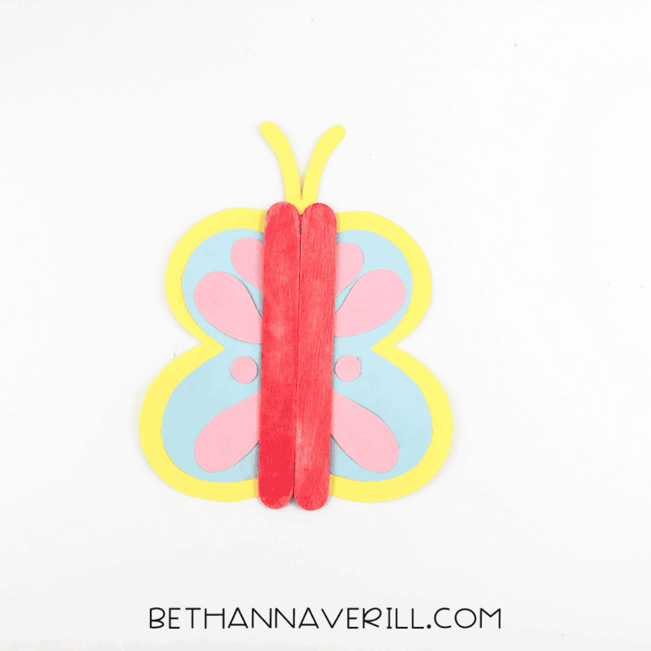 Completed butterfly popsicle stick craft with red body, yellow antennae, and layered cardstock wings on a white background.