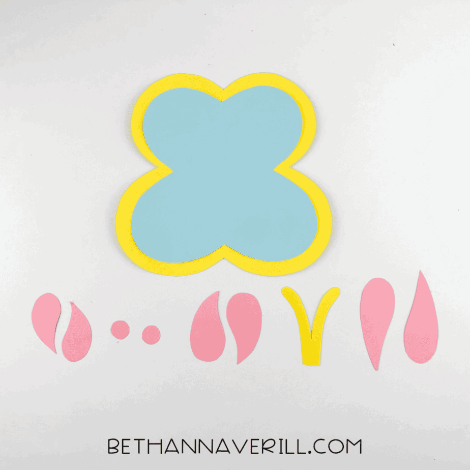Layered butterfly wing shapes assembled from yellow and blue cardstock, with pink wing details placed on top.