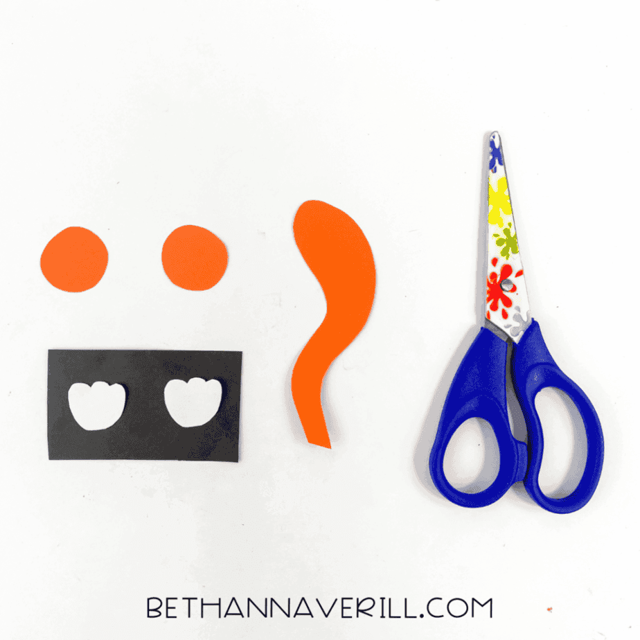 Small orange paper circles, a curved orange paper tail shape, and black cardstock with two white paw cutouts on a white background.