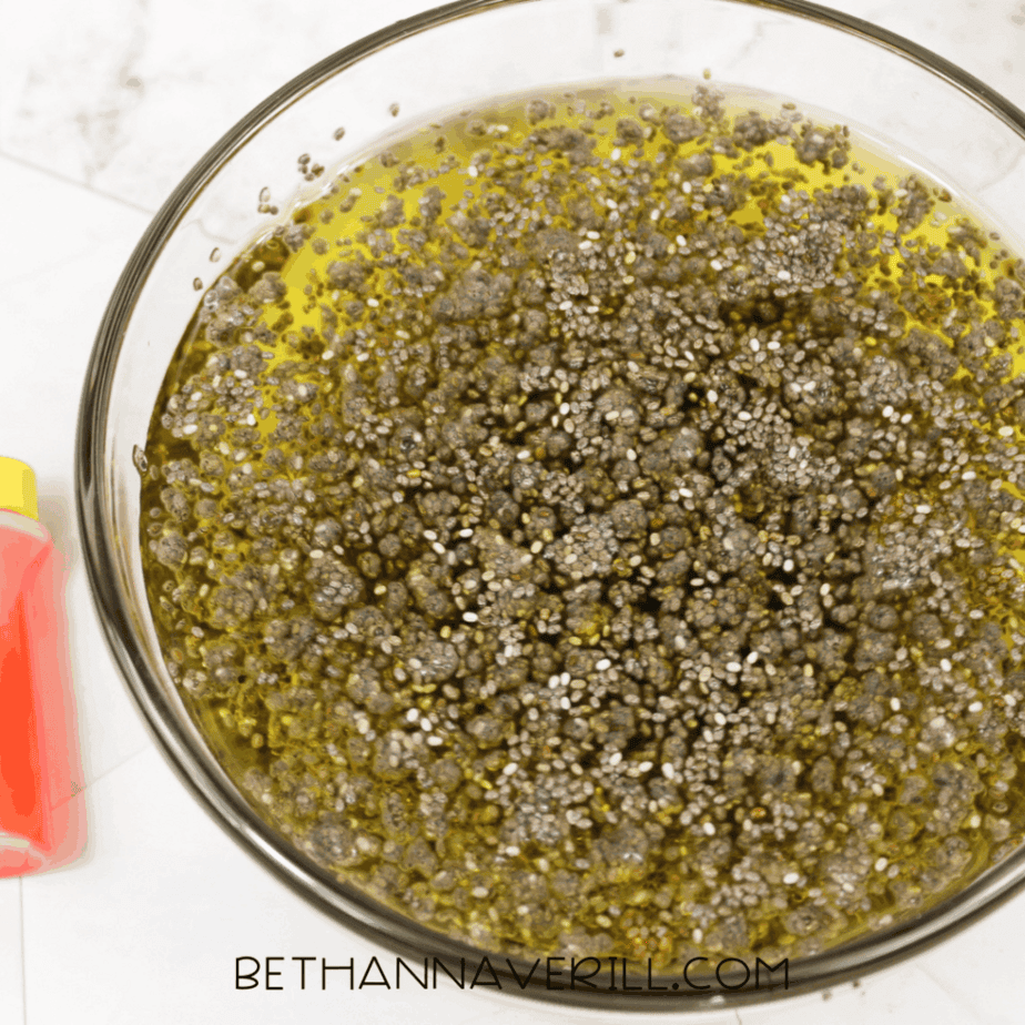Glass bowl filled with hydrated chia seeds tinted yellow, shown from above on a white surface.
