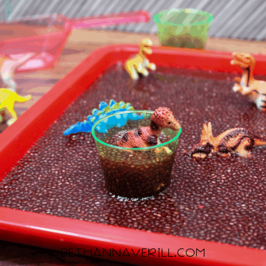 Small clear cup filled with hydrated chia seeds and a plastic dinosaur partially submerged inside.
