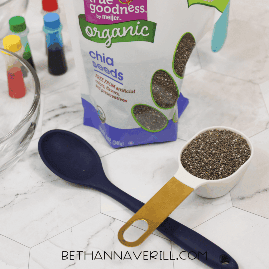 Measuring cup filled with dry chia seeds placed next to a spoon and an open bag of chia seeds.