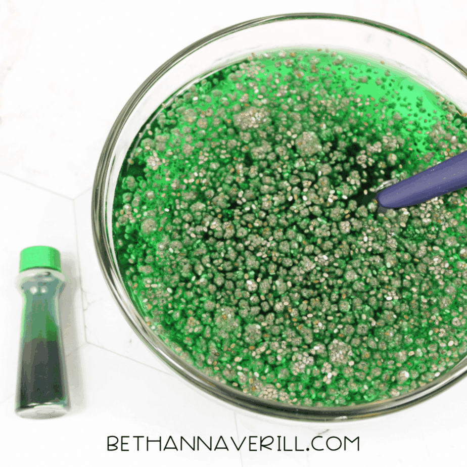 Glass bowl filled with chia seeds and green-tinted liquid being stirred with a spoon.
