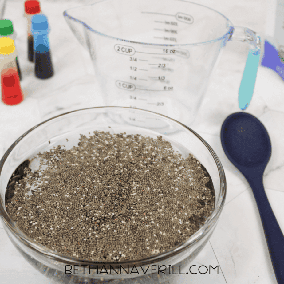 Glass bowl filled with chia seeds and water, shown from above with a measuring cup and spoon nearby.