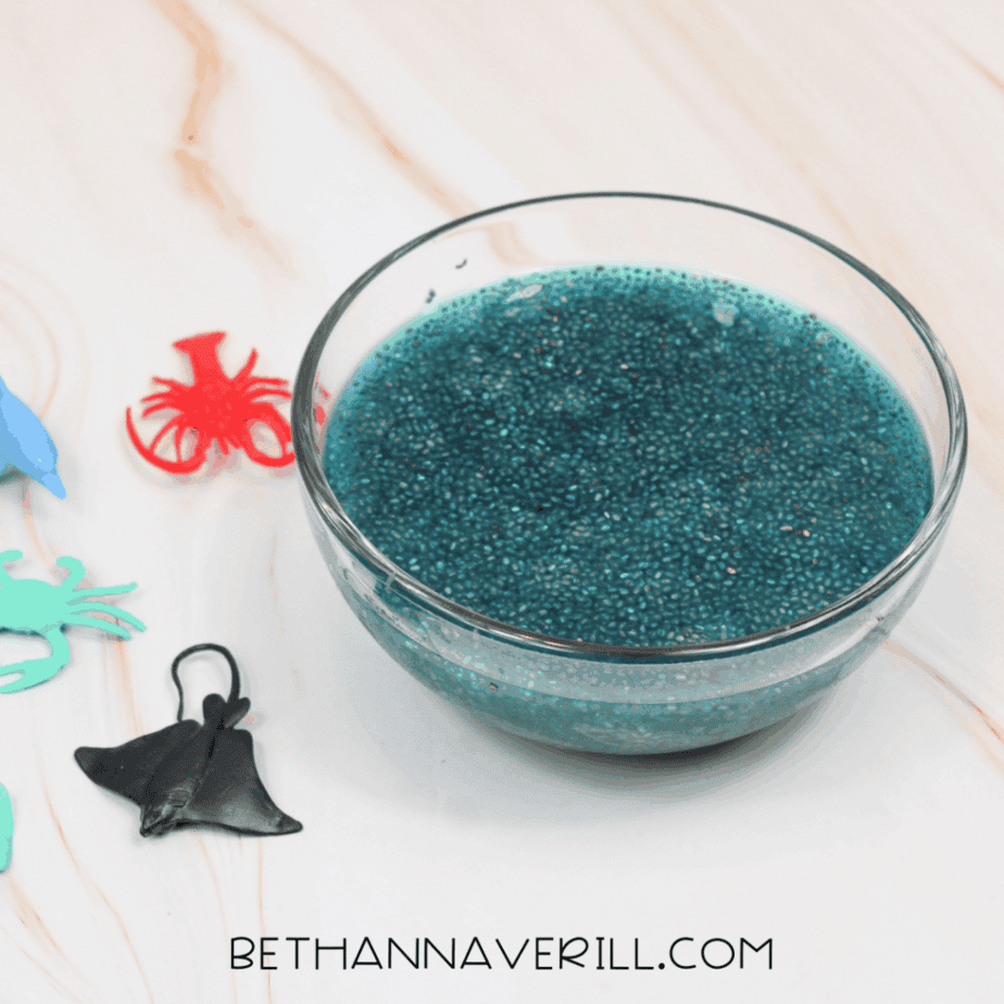 Glass bowl of blue-tinted hydrated chia seeds on a white surface with plastic ocean animal toys placed nearby.