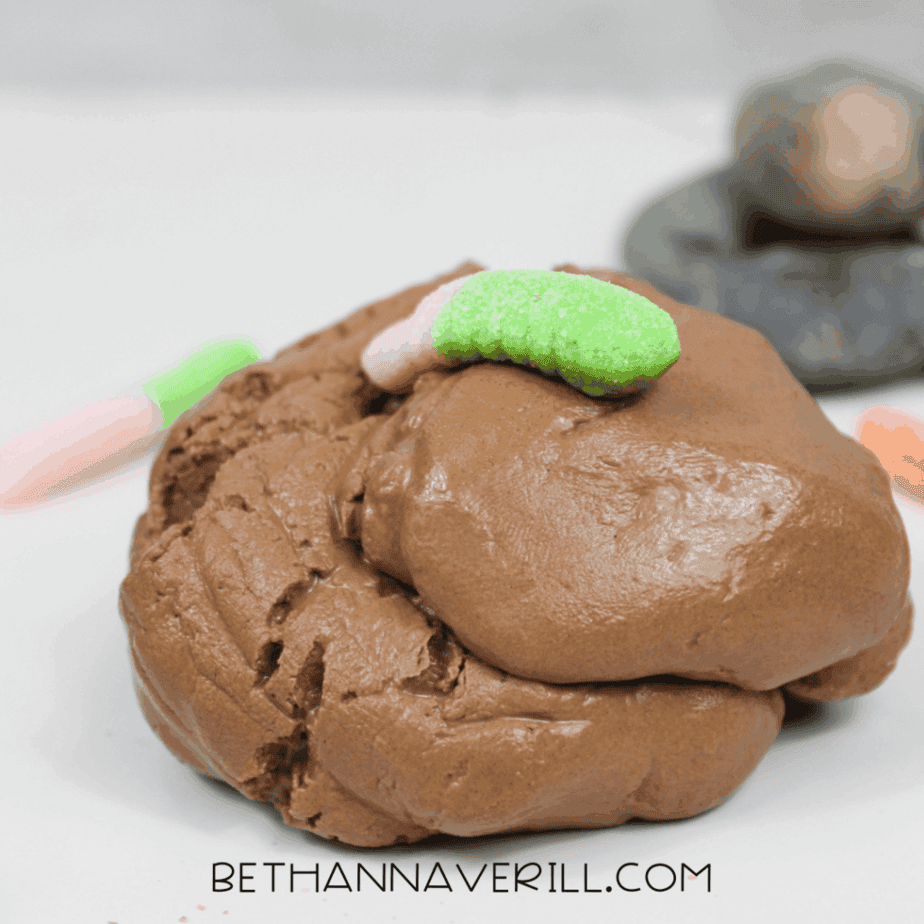 Brown slime mixture on a white surface with a gummy worm placed on top and rocks visible in the background.