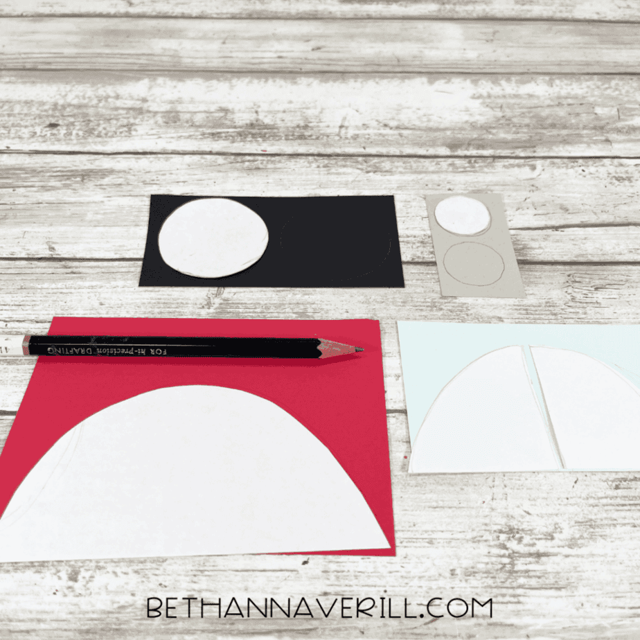 Cardstock pieces cut into circles and half circles for wheels and car windows, with a pencil and scissors on a white wood background.