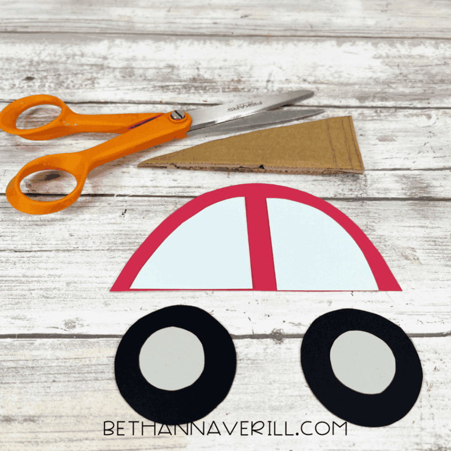 Cardboard triangles cut out for the car roof with scissors and cardstock window pieces nearby.