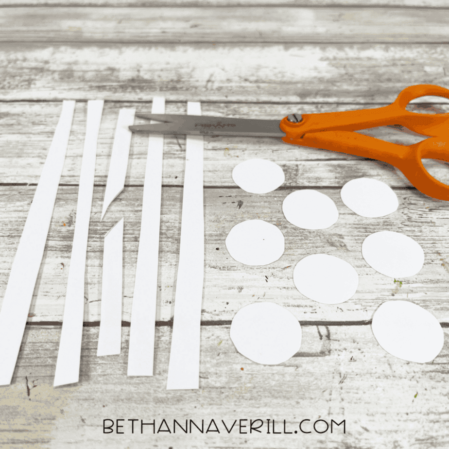 Two cardstock squares decorated with white circles and diagonal white stripes, placed side by side with scissors on a white wood background.