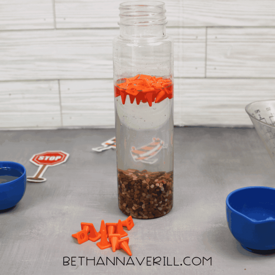 Clear plastic bottle filled with water and pebbles, with orange plastic traffic cones floating near the surface inside the bottle.