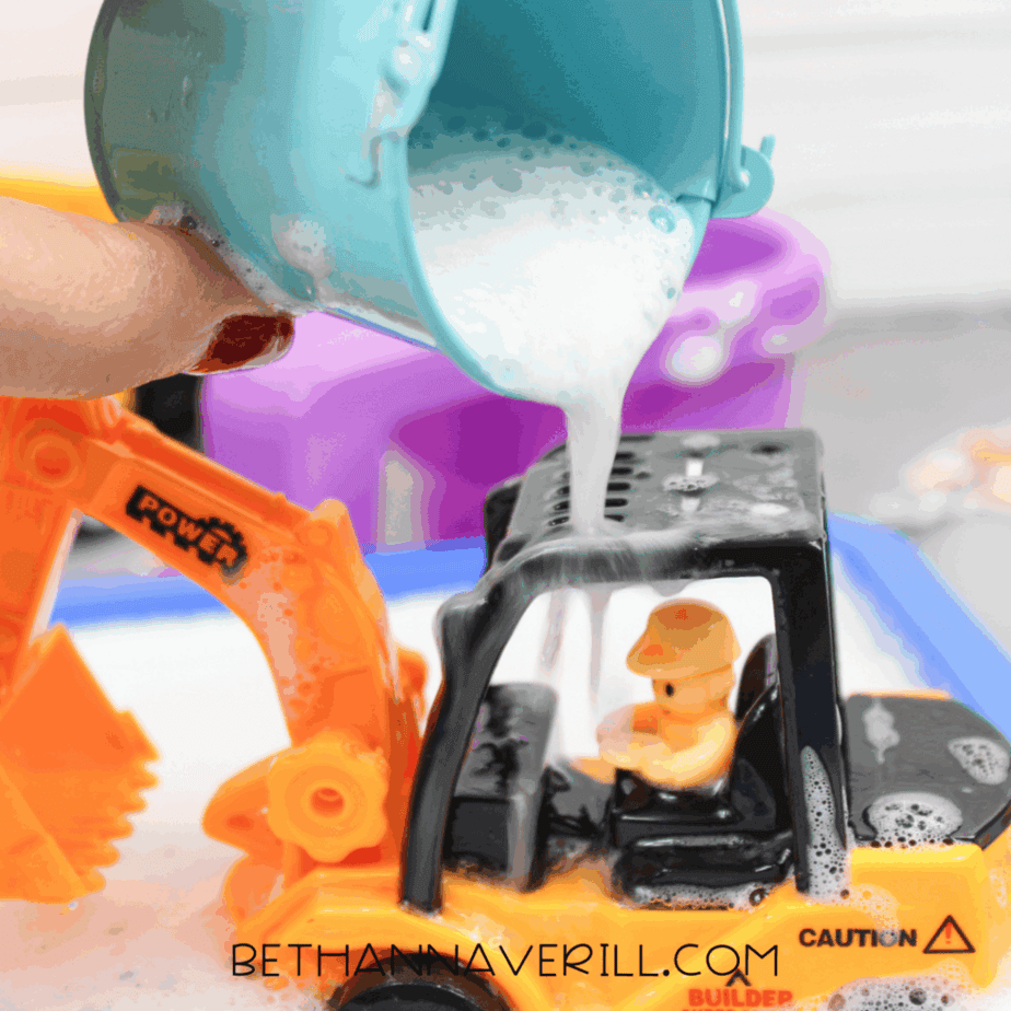 Completed construction sensory bin with sand tray, bubble wash station, toy trucks, scoops, and rocks.