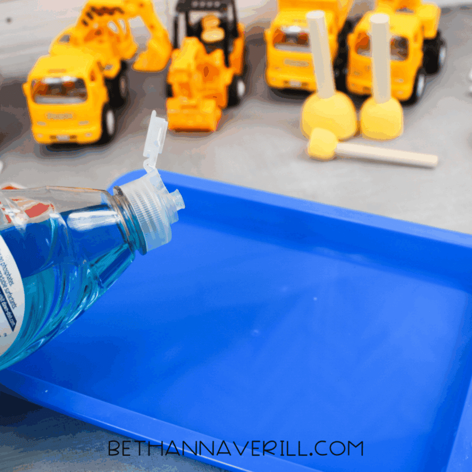 Blue tray as bubble solution is poured in to create a wet sensory area for washing construction vehicles.