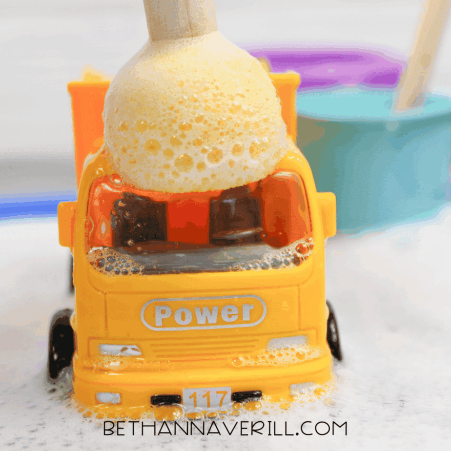 Foamy bubble mixture poured onto a toy excavator during construction sensory play.
