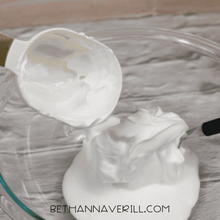 Shaving cream being scooped from a measuring cup and added into a clear glass mixing bowl.